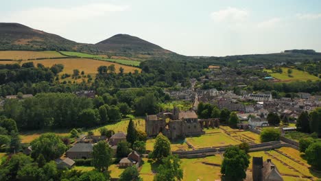 Epic-shot-of-majestic-Melrose-Abbey-historic-ruins-with-farming-fields-at-the-foreground-in-Melrose,-Scotland