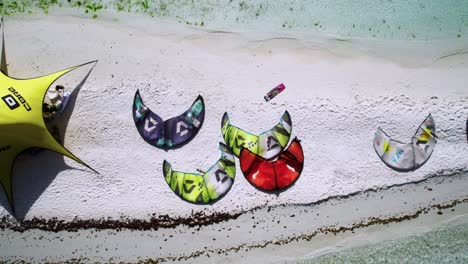 Colorful-kites-on-white-sandy-beach-from-above,-bright-sunny-day