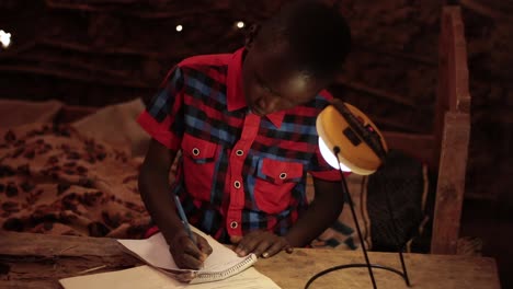 Un-Joven-En-Kenia-África-Estudiando-En-Casa-Usando-Una-Lámpara-Solar-En-Una-Casa-De-Barro