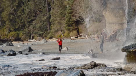 Una-Pareja-Con-Su-Perro-Caminando-Por-La-Orilla-Y-Tomando-Fotografías-En-La-Pequeña-Cascada-Que-Corre-Sobre-El-Acantilado-En-Mystic-Beach-En-La-Isla-De-Vancouver,-BC,-Canadá