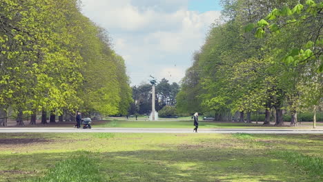 A-Shot-Of-Kungsparken-In-Malmo-with-the-Pegasus-statue,-surrounded-by-trees,-as-people-walk-and-a-car-drives-by