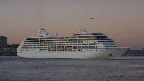 Starboard-View-Of-Passenger-Cruise-Ship-On-The-River-Hudson-With-Bird-Flying-Past-During-Sunset