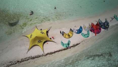 Colorful-kites-and-a-yellow-tent-on-a-sandy-beach-by-clear-turquoise-waters