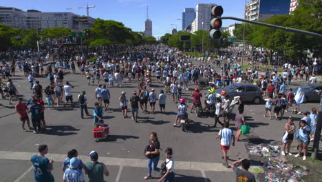 Drone-shot-of-traffic-Jam-at-9-de-Julio-Avenue,-crowded-with-football-soccer-fans-and-street-vendors,-they-notice-drone-camera,-wave-flags