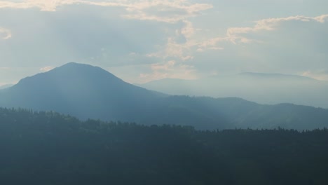 Aerial-shot-showing-layered-mountain-ridges-covered-in-mist-and-sun-rays,-cloudy-day