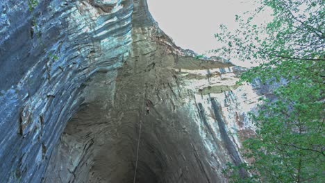 Bungee-jumper-falls,-bounces-and-swings-under-huge-cave-entrance