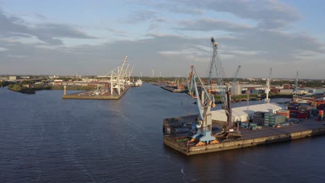 Pan-around-drone-view-of-industrial-buildings-of-harbor-in-Hamburg-with-container-cranes-located-on-cloudy-day-in-modern-city-on-river