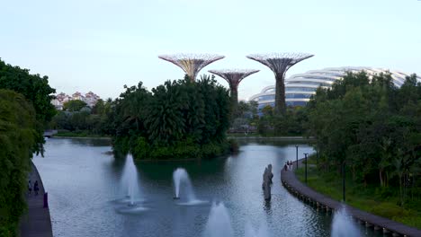 people-strolling-at-Gardens-by-the-Bay-near-a-lake-with-super-trees-in-the-background-and-small-water-fountains