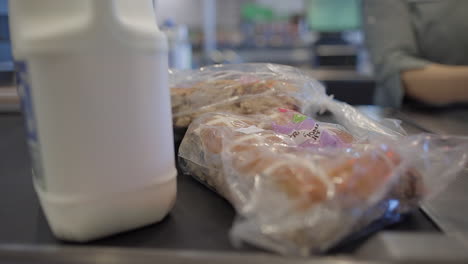 Up-close-shot-of-food,-Easter-buns-and-milk-being-on-the-conveyor-belt-about-to-be-scanned-scanned-in-a-shopping-centre,-all-or-supermarket-by-a-shop-employee