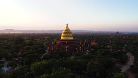 Flying-over-the-countryside-of-Myanmar-looking-at-the-beautiful-golden-yellow-Dhammayazaka-Pagoda,-a-popular-Buddhist-temple---Aerial-shot