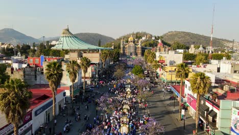 Panoramic-aerial-view-of-a-pilgrimage-to-the-Basilica-of-Guadalupe-and-the-expiatory-temple-of-Christ-the-King,-Mexico-City-on-a-sunny-day,-roadway-lined-with-jacaranda-trees