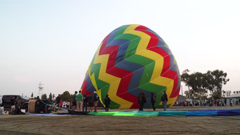 Ein-Bunter-Heißluftballon-Wird-Zur-Vorbereitung-Auf-Den-Start-Mit-Luft-Gefüllt,-Während-Eine-Menge-Zuschauer-Zusieht