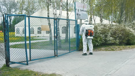 Man-in-protective-suit-disinfecting-gates-and-public-space-with-a-spray-gun