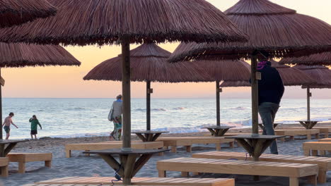 Beautiful-sunset-beach-with-sun-beds,-tiki-umbrellas,-sea-view,-sand-and-kids-playing,-people-walking,-holiday-vacation-in-Marbella-Spain,-4K-shot