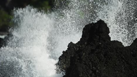 Wellen-Brechen-Gegen-Schwarze-Lavasteine-An-Der-Küste-Von-Maui-Mit-üppigem-Grün-Im-Hintergrund