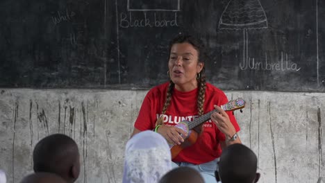 Caucasian-volunteer-playing-ukelele-music-in-an-African-school-with-kids-looking-to-her