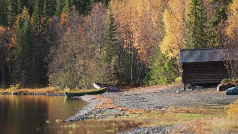 Ruhige-Ufer-Eines-Herbstwaldes,-Wo-Zwei-Boote-Friedlich-Auf-Einem-Kieselstrand-Liegen,-Inmitten-Der-Leuchtenden-Farben-Des-Herbstlaubs