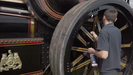 A-man-cleaning-the-rear-wheel-of-a-black-vintage-traction-engine-with-a-cloth