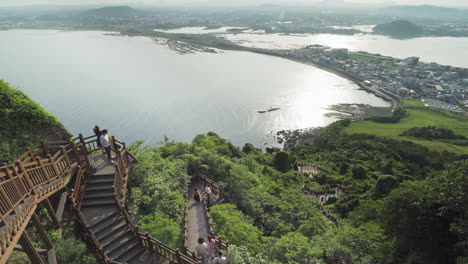 Tourists-descend-stairs-at-Seongsan-Ilchulbong-Peak-in-the-afternoon,-Jeju-Island,-South-Korea,-high-angle-wide-pan-right-in-4K