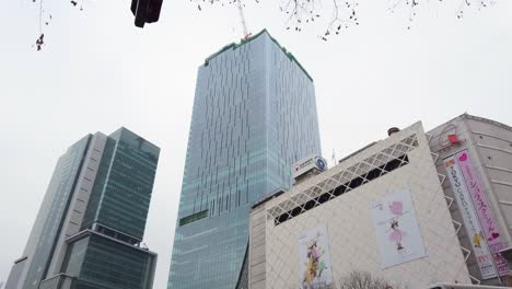 Die-Vorderseite-Des-Bahnhofs-Shibuya-Wird-Langsam-Nach-Unten-Geschwenkt,-Im-Hintergrund-Sind-Das-Shibuya-Scramble-Square-Gebäude-Und-Das-Hikarie-Gebäude-Zu-Sehen