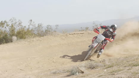 SLOW-MOTION:-A-dirt-biker-rides-his-dirt-bike-through-the-desert-and-whips-around-a-berm