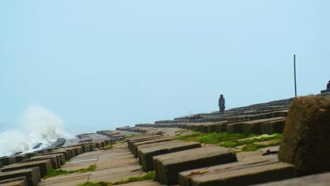 Un-Hombre-Se-Para-Y-Camina-Al-Borde-De-Un-Terraplén-De-Hormigón-Mientras-Las-Olas-Golpean-La-Costa-De-Kuakata,-Bangladesh