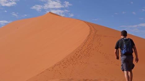 Man-start-to-climb-a-beautiful-dune-in-Namib-Naukluft-National-Park,-Namibia