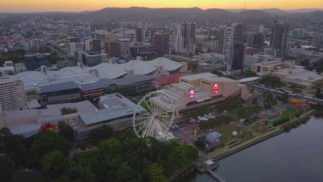 Aerial-top-down-view-of-a-modern-city-Ferris-wheel-by-the-river-at-sunset