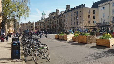 Gente-En-Bicicleta-Por-Las-Calles-Históricas-De-La-Ciudad-De-Oxford-Con-Vistas-Al-Teatro-Sheldonian-En-La-Distancia,-Inglaterra