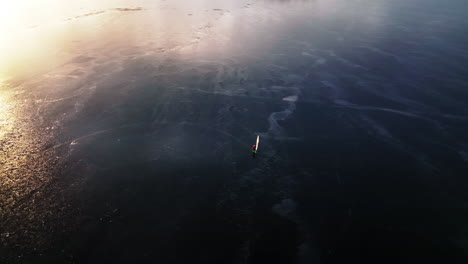 Aerial-view-of-ice-windsurfer-turning-clockwise-on-frozen-lake-in-sunset