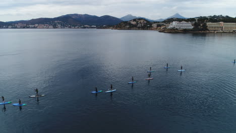 Toma-De-Drone-De-Un-Grupo-De-Personas-Usando-Remos-De-Pie-En-El-Mar,-4k-Uhd