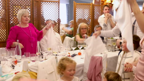 big-family-fest-in-a-restaurant-waving-white-towels-in-the-air-celebrating-first-communion