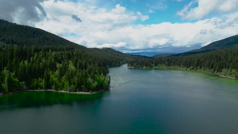 Drone-footage-of-a-mountain-lake-in-Canada-with-blue-and-green-water,-coniferous-forests,-and-forest-houses-on-the-shore