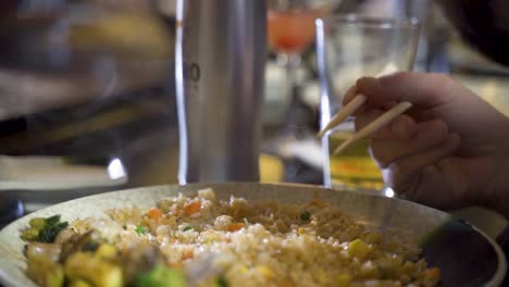 Bearded-man-eating-fried-rice-with-chop-sticks-at-dinner-table,-slow-motion