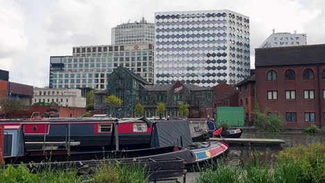 Urban-street-view-overlooking-canal-with-boats-at-Regency-Wharf-and-skyscraper-buildings-in-the-city-centre-of-Birmingham,-the-midlands-of-England-UK