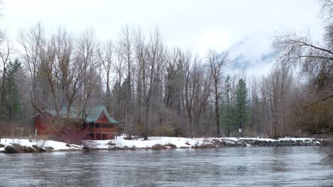 Cascade-Mountain-Pass-to-Leavenworth,-Washington---A-beautiful-Bavarian-styled-alpine-village-covered-in-snow---Panning-left-on-wooden-cabin-and-rushing-river---Beautiful-crisp-water