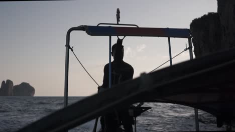 Silhouette-of-man-driving-motorboat-for-tourists,-sightseeing-cliff-islands-during-sunset,-Phi-Phi-Island,-Thailand