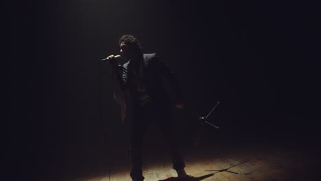 man-in-suit-singing-under-dramatic-light-on-slow-mo