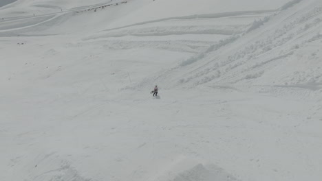 Drone-view-of-snowboarder-walking-on-the-pistes-on-the-snowy-slopes-of-Mount-Hermon,-Golan-Heights,-Israel,-flying-forward