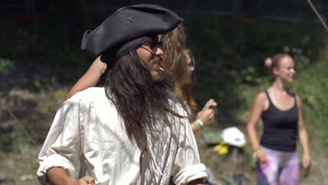 Man-with-pirate-hat-and-white-shirt-dancing-on-beach-on-group-party,-sunny-summer-day