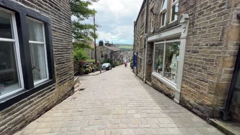 Walking-along-Haworth-Main-Street-with-cobbled-road-and-and-people-walking-along-shopping-and-filled-with-tourists