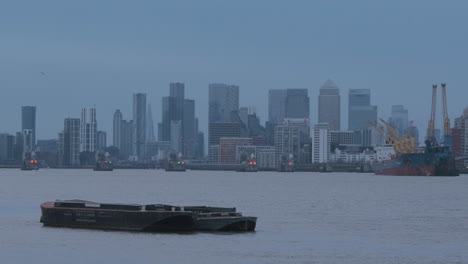 Vista-Industrial-Del-Támesis-Con-Barco,-Barrera-De-Mareas-Del-Támesis-Y-Canary-Wharf,-Paisaje-Urbano