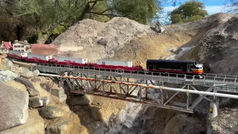 Miniature,-toy-train-set-over-a-bridge,-waterfall-and-rocky,-old-wes-landscape