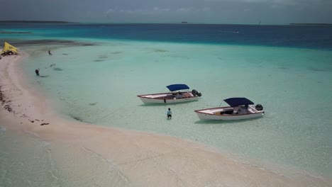 Two-boats-anchored-in-turquoise-waters-near-a-sandy-beach-on-a-sunny-day,-aerial-view