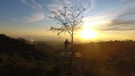 Man-playing-violin-on-viewpoint-in-Batu-Dulang,-Indonesia-on-scenic-sunrise