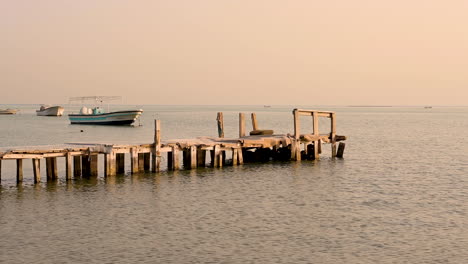 Antiguo-Muelle-De-Madera-Sobre-Hermosas-Y-Tranquilas-Olas-De-Agua-De-Mar-Con-Barcos-En-El-Fondo-Sobre-El-Cielo,-Bahrein