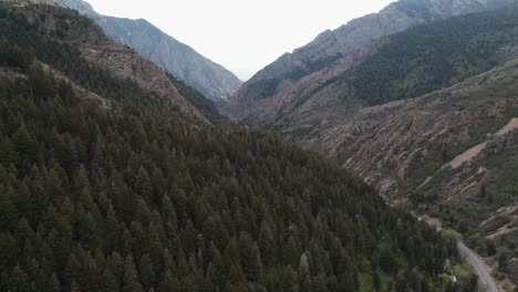 Zooming-out-shot-while-panning-up-of-Big-Cottonwood-canyon-road-in-Utah-with-a-vast-background-of-sunset-lit-mountains