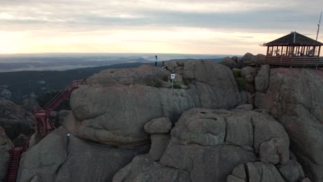 Luftaufnahme-Einer-Frau-Auf-Einem-Felsigen-Hügel-Mit-Glasfenstern-Und-Herrlichem-Blick-Auf-Die-Bergkette