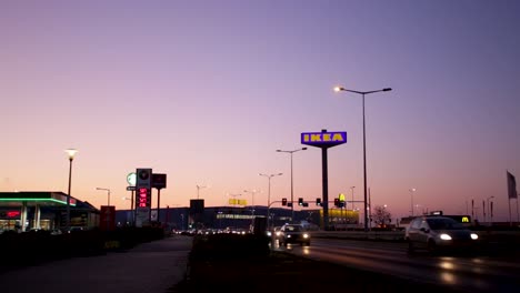 Eine-Abendliche-Landschaft-Mit-Lichtern,-Die-Die-Stadt-Erhellen-Und-Fahrenden-Autos,-Die-An-Der-Autobahn-Vorbeifahren---Ruhige-Aufnahme