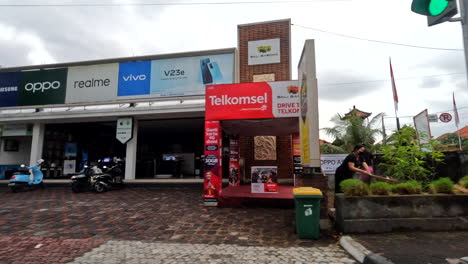 POV-driving-past-shop-fronts,-buildings-and-people-on-mopeds-in-Bali,-Indonesia